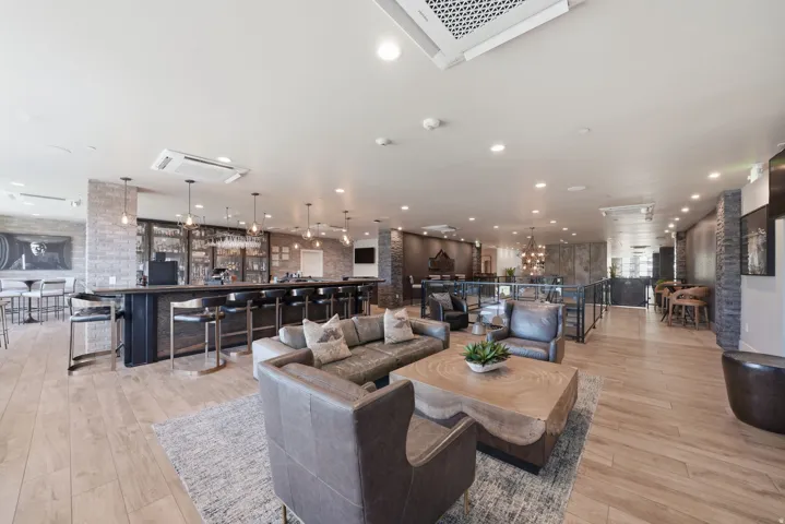 Spacious common area featuring a full-service bar with pendant lighting, light wood-finish flooring, and recessed lighting