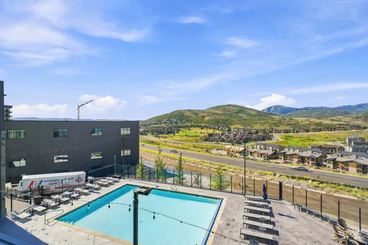 Resort-style rooftop pool deck with turquoise saltwater pool, glass fencing, lounge seating areas, and panoramic vistas of rolling hills and the surrounding valley landscape