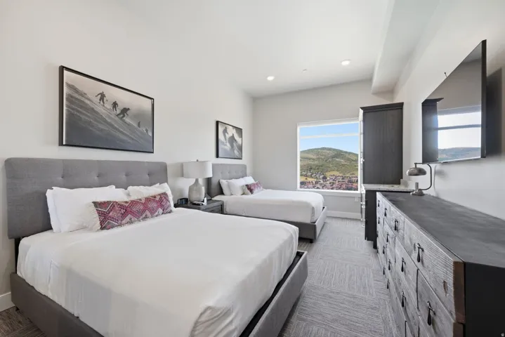 Spacious guest bedroom featuring two queen beds with upholstered headboards, soft white bedding, and decorative accent pillows