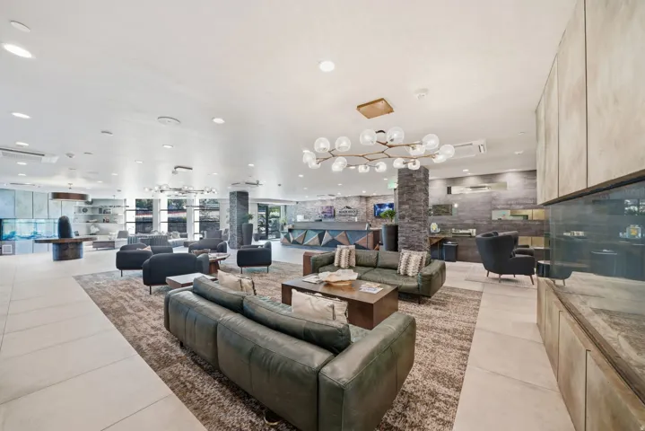 Spacious open-concept lounge featuring polished tile flooring, a modern chandelier with multiple globe pendant lights, built-in cabinetry with wood-finish detailing, and a striking brick accent wall