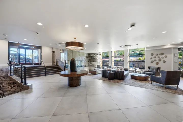 Sophisticated lobby featuring polished tile flooring, recessed and pendant lighting throughout, floor-to-ceiling windows with natural light, and a striking wood-finish accent column anchoring the central space