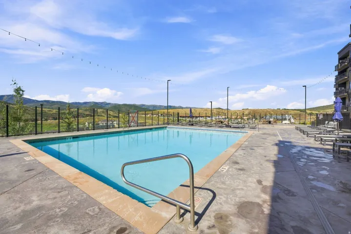 Expansive outdoor pool with concrete decking, perimeter fencing, and string lighting