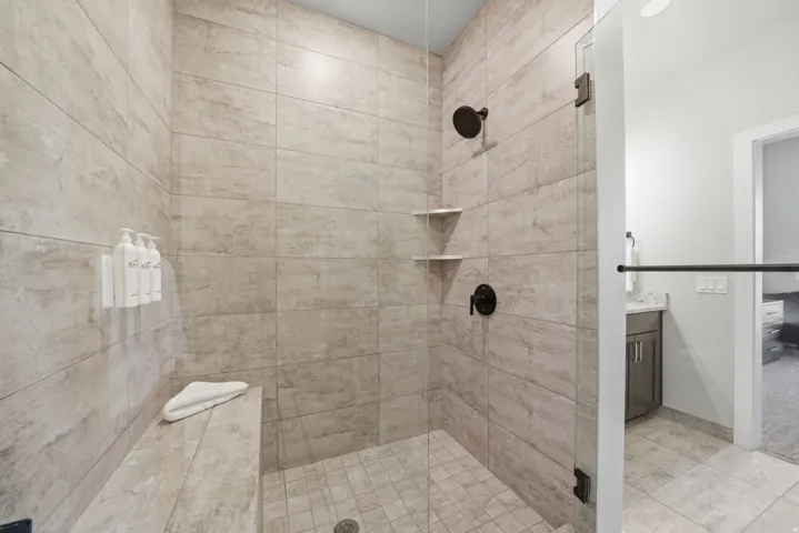 Spa-inspired walk-in shower featuring linear tile detailing, frameless glass enclosure, dual showerheads with individual controls, built-in corner shelving, and a spacious layout with tile flooring throughout
