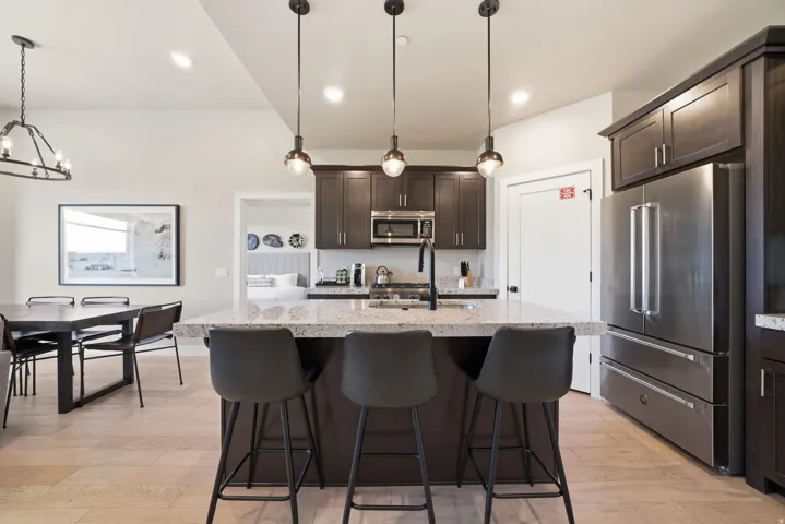 Contemporary kitchen and dining area featuring a large center island with waterfall-edge countertop, three pendant lights with adjustable cords, and seating for multiple guests