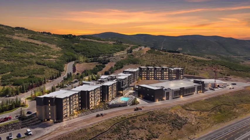 Modern multi-story buildings with balconies, an outdoor swimming pool, and dedicated parking areas, set against a mountainous landscape