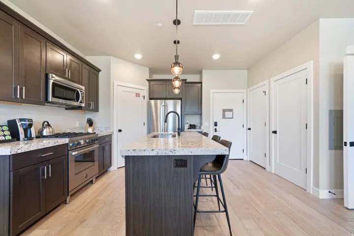 Chef's kitchen featuring dark cabinetry with stainless steel appliances, quartz countertops, a large center island with seating, pendant lighting, wood-finish flooring, and abundant natural light from recessed ceiling fixtures