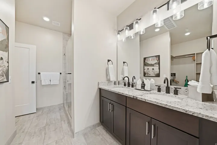 Spa-inspired primary bathroom featuring a dual-sink vanity with stone countertop, dark cabinetry with chrome hardware, and polished chrome faucets