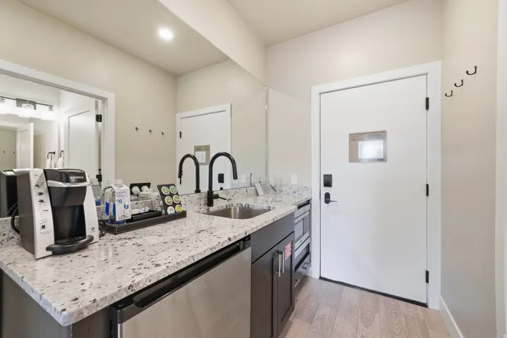 Kitchenette featuring granite countertops, stainless steel sink with matte black faucet, integrated beverage refrigerator, and built-in microwave
