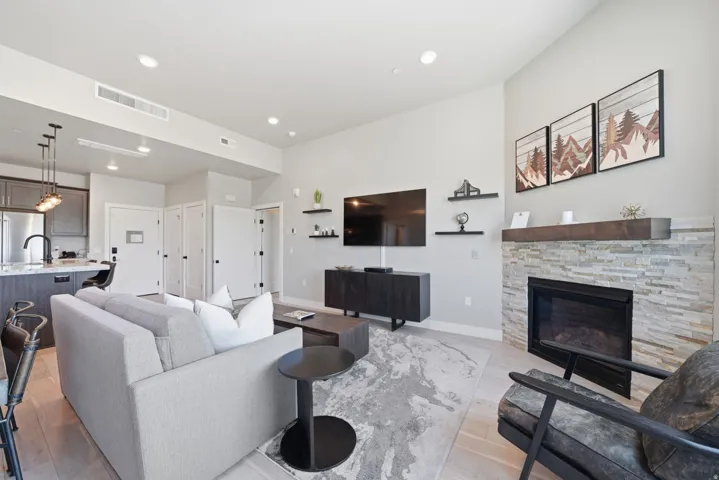 Contemporary living space featuring a gas fireplace with stacked stone surround, recessed ceiling lighting, and wood-finish flooring throughout