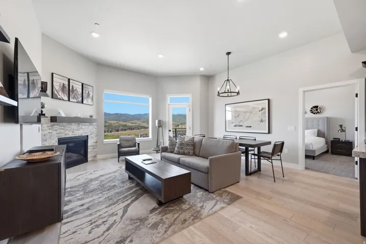 Open-concept living area with light wood-finish flooring, a stone-clad fireplace, and a dining area featuring a dark-finish table