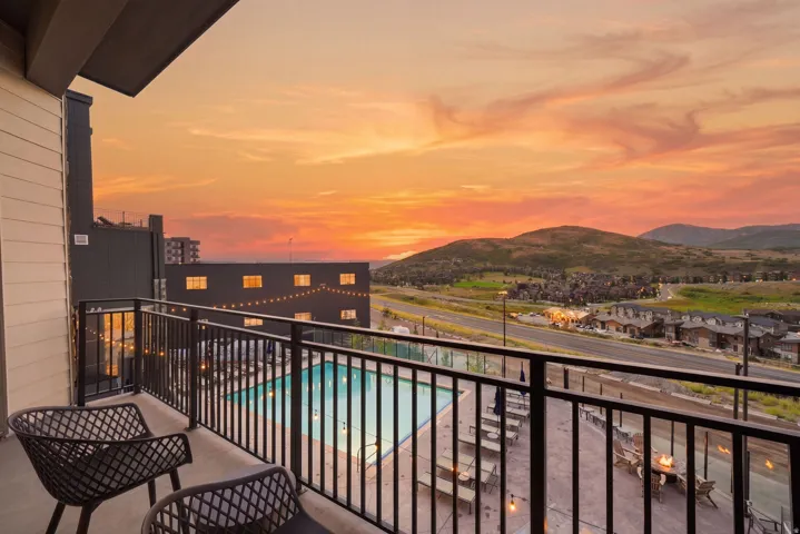 Elevated balcony with metal railing and modern seating area overlooking expansive valley landscape, mountain ranges, and illuminated residential community below