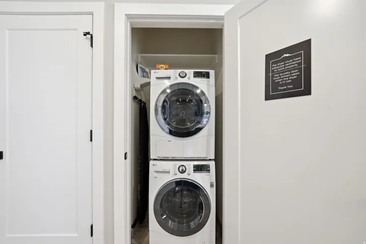 Dedicated laundry closet featuring stacked front-load washers and dryers with modern digital controls, white cabinetry, and bright recessed lighting for efficient garment care
