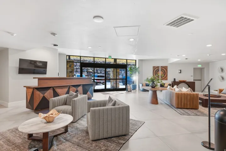 Modern lobby and lounge area featuring polished tile flooring, recessed ceiling lighting, and floor-to-floor glass entry doors with black framing