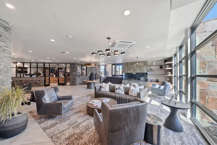 Open-concept living space featuring recessed ceiling lighting, large multi-panel glass doors and windows with natural light, neutral wood-finish flooring, built-in shelving and cabinetry, and a modern ceiling fan with integrated lighting fixture