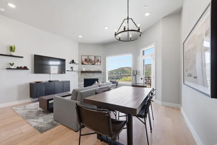 Open-concept living and dining area featuring hardwood flooring, a wood-finish dining table with seating for six, and a fireplace with stone surround