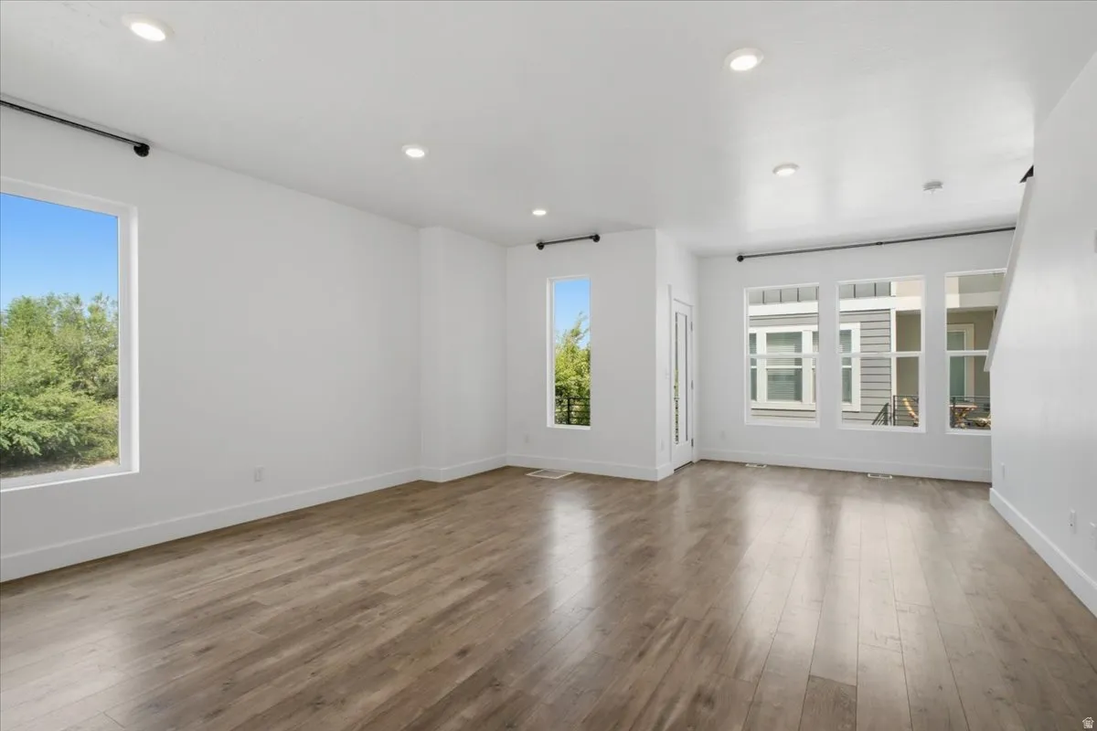 Spacious room with wood-finish flooring, recessed lighting, multiple windows, and crisp white walls
