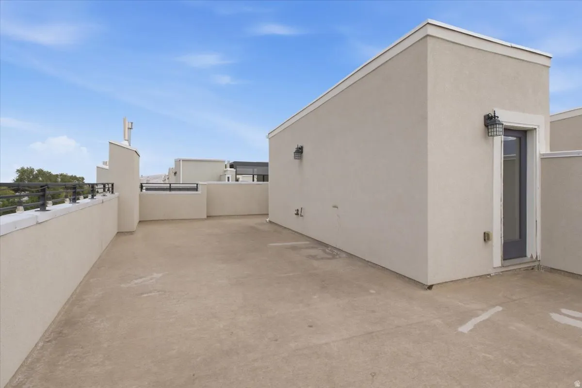 Expansive rooftop patio with concrete flooring, stucco exterior walls, and black metal railings