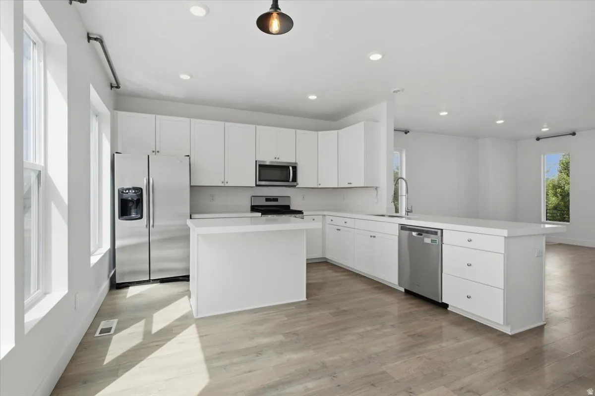 Kitchen featuring white cabinetry, stainless steel appliances, a center island, and wood-finish flooring
