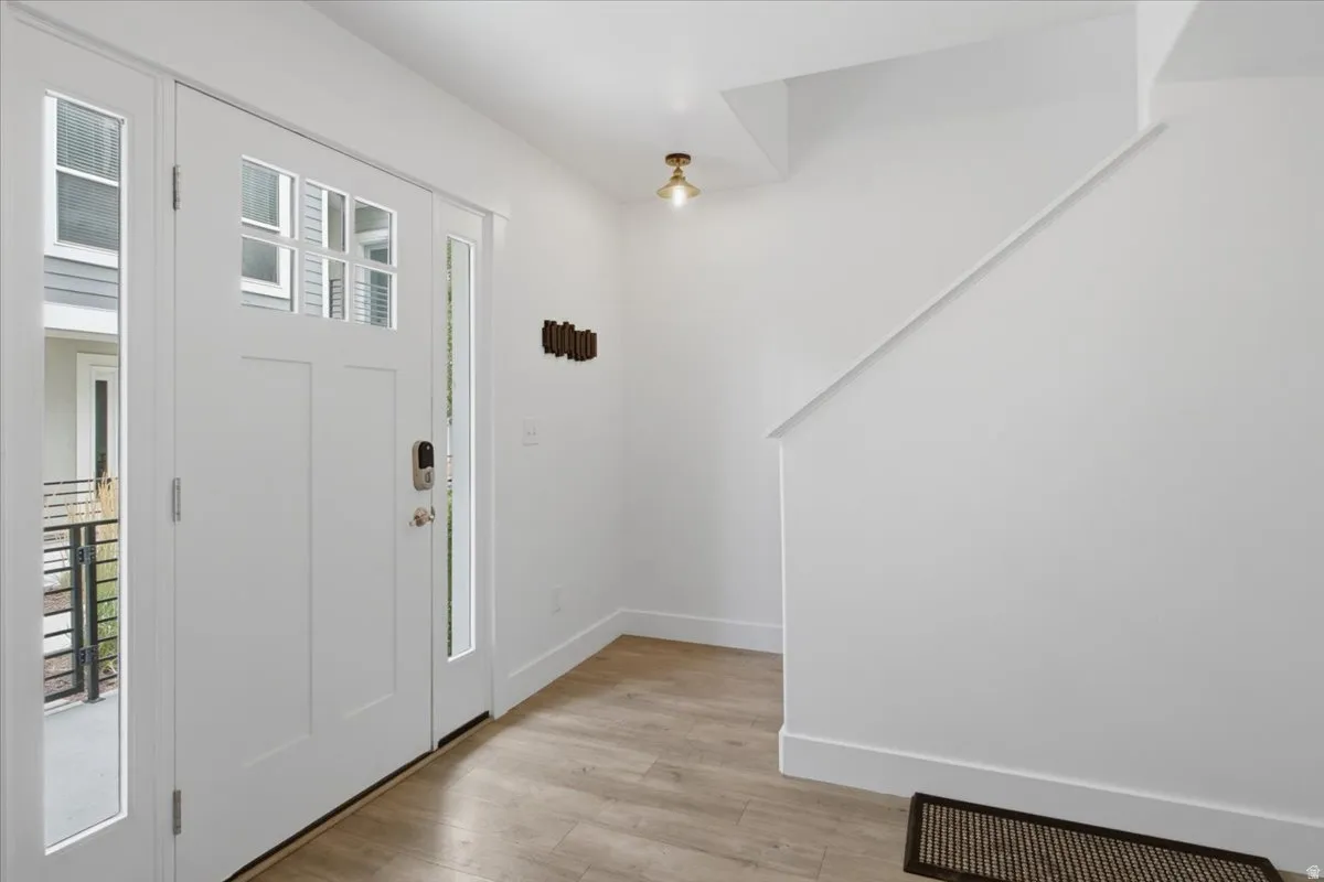 Entryway featuring wood-finish flooring, a white paneled door with glass inserts, and white walls