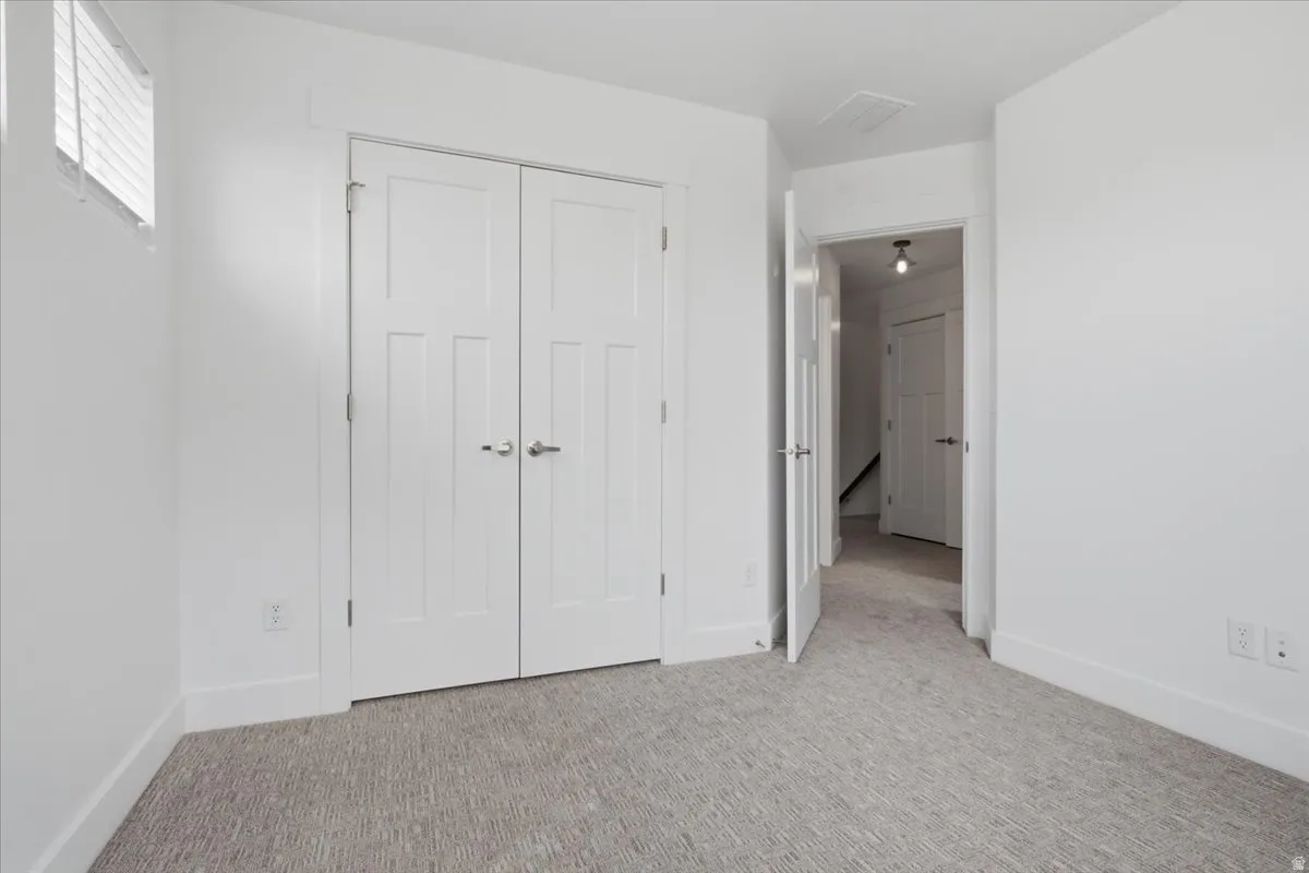 White painted walls, light-colored patterned carpeting, white interior doors, and a window with horizontal blinds