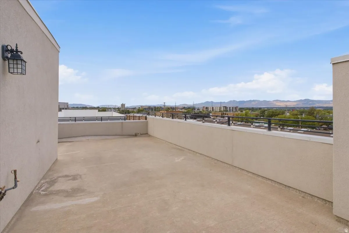 Expansive rooftop deck with panoramic scenery, featuring a concrete surface, stucco walls, and a black metal railing