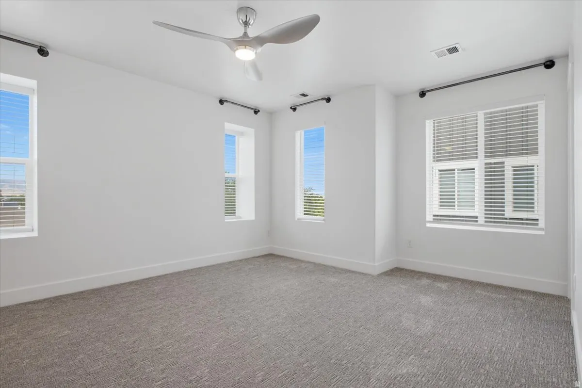 Recessed-panel windows with blinds, gray carpeting, white walls, and a modern ceiling fan with integrated lighting