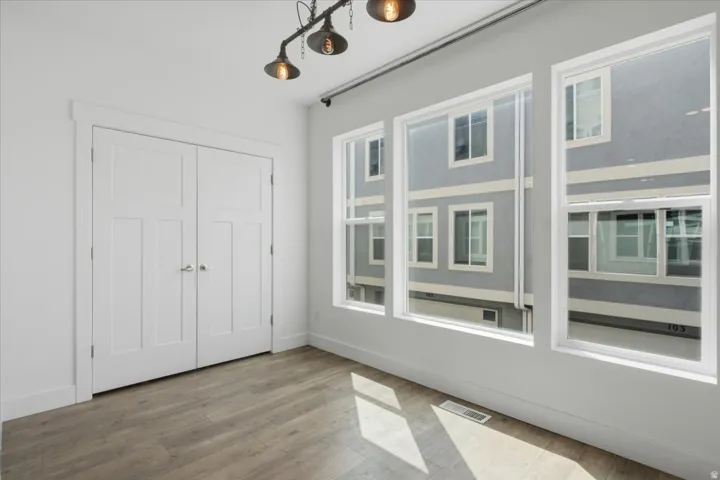 Wood-finish flooring, white walls, industrial-style ceiling light fixture, three vertical windows, and white paneled bi-fold doors