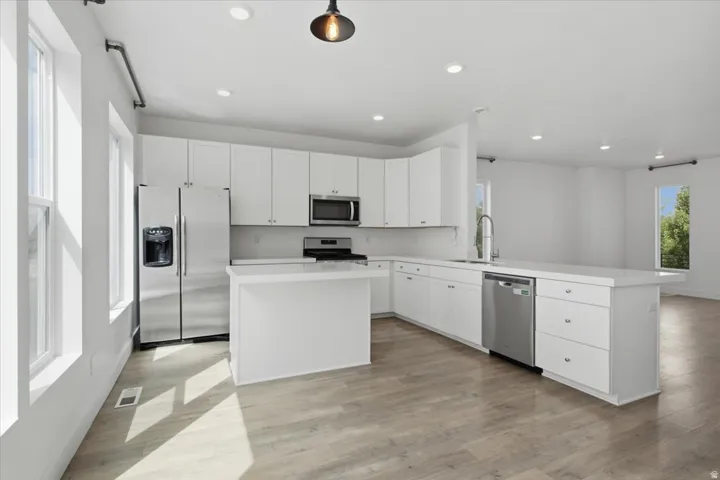 Kitchen featuring white cabinetry, stainless steel appliances, a center island, and wood-finish flooring