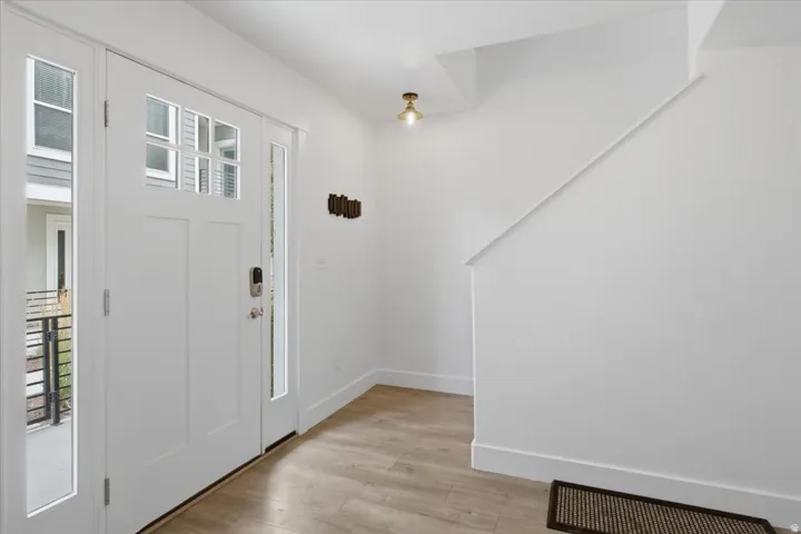 Entryway featuring wood-finish flooring, a white paneled door with glass inserts, and white walls