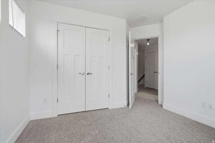 White painted walls, light-colored patterned carpeting, white interior doors, and a window with horizontal blinds