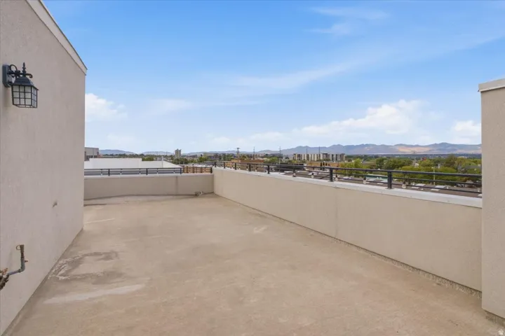 Expansive rooftop deck with panoramic scenery, featuring a concrete surface, stucco walls, and a black metal railing