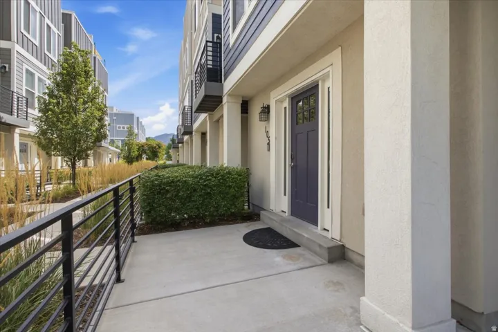 Entry porch with concrete surface, black metal railing, and manicured shrubbery