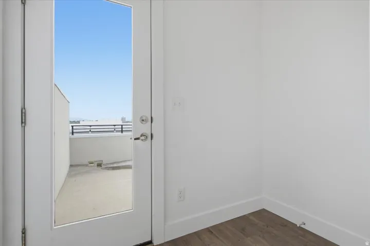 Full-lite door leading to an outdoor balcony with a concrete surface and metal railing, complemented by wood-finish flooring indoors
