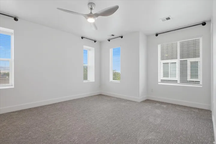 Recessed-panel windows with blinds, gray carpeting, white walls, and a modern ceiling fan with integrated lighting