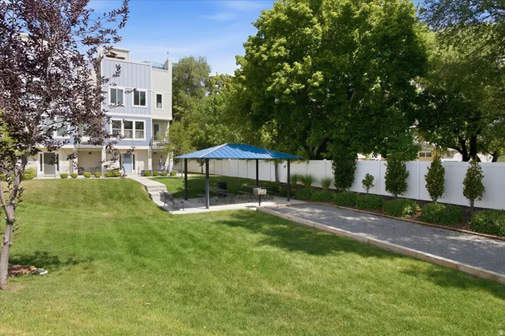 Expansive lawn area with a gravel pathway, a blue-roofed gazebo, mature trees, and a white privacy fence