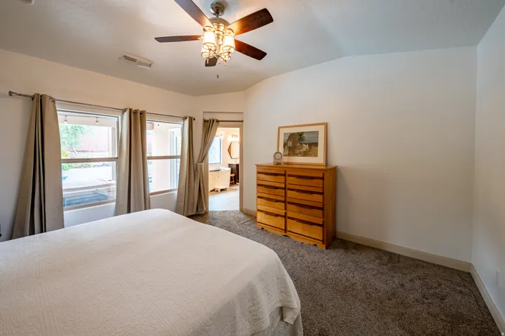 Vaulted ceiling with a ceiling fan, carpeted flooring, and multiple windows