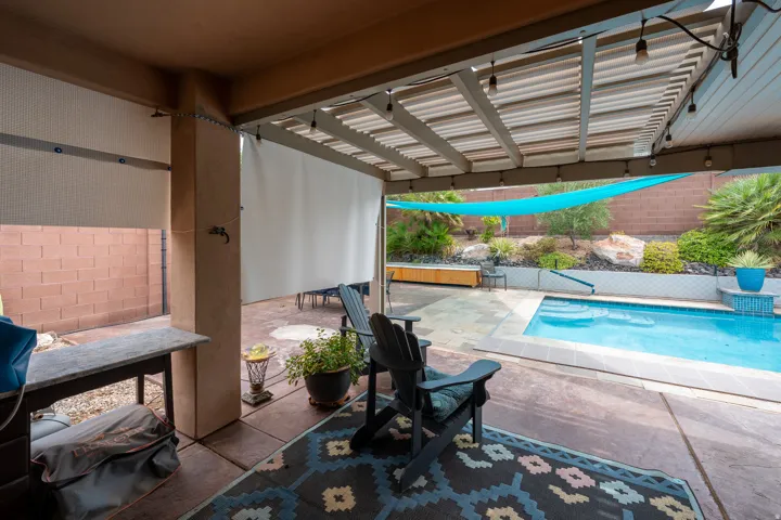 Covered patio with roll-down shades, stamped concrete flooring, string lighting, and a built-in swimming pool with a water feature