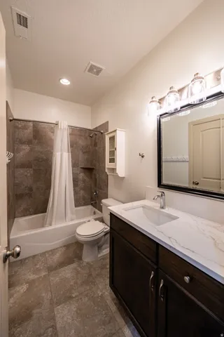 Full bathroom featuring a dark wood-finish vanity with a light-toned countertop, a framed mirror with a four-light fixture, a built-in medicine cabinet, and a tiled shower with a bathtub