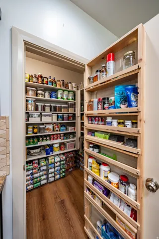 Walk-in pantry featuring built-in shelving, door-mounted spice racks, and wood-finish flooring