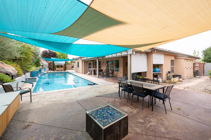 Expansive patio featuring a built-in swimming pool, concrete hardscaping, multiple shade sails, and a built-in fire pit