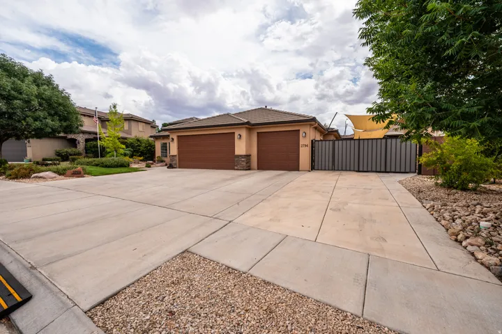 Stucco exterior with stone accents, two-car garage, concrete driveway, and side gate access