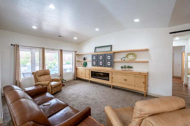 Vaulted ceiling with recessed lighting, integrated entertainment center with floating shelves, fireplace, multiple windows, and carpeted flooring