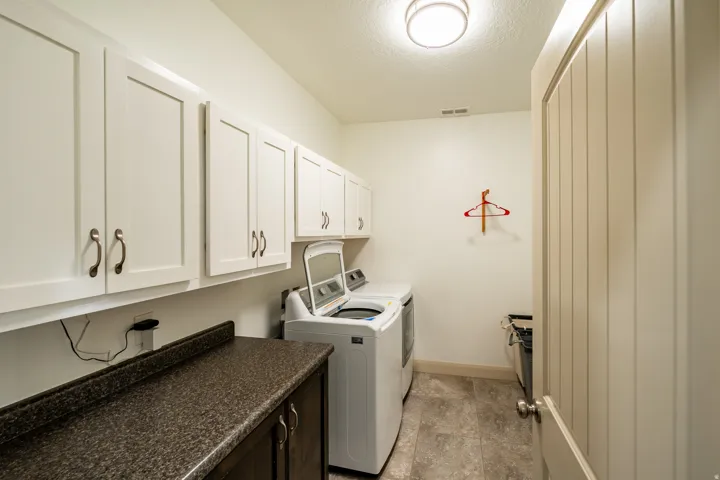 Functional laundry area featuring white shaker-style cabinetry, dark countertops, and tile flooring