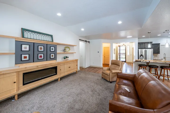 Built-in media console with fireplace, open shelving, vaulted ceiling, recessed lighting, and wood-finish flooring