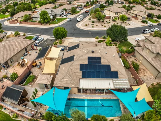 In-ground swimming pool with shade sails, solar panel array, covered patio, and perimeter fencing