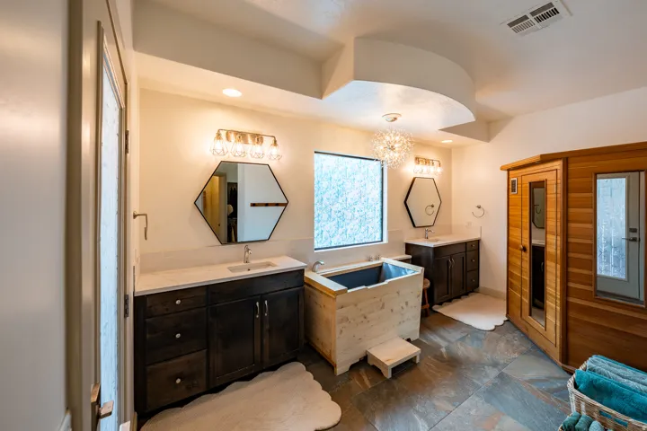 Dual dark wood-finish vanities with light countertops, freestanding wooden soaking tub, built-in wooden sauna, and slate tile flooring