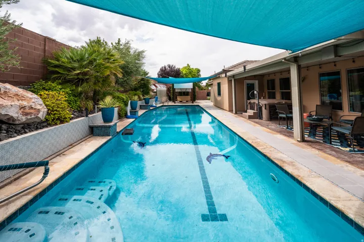Outdoor swimming lane with integrated steps, shaded patio area, and mature landscaping