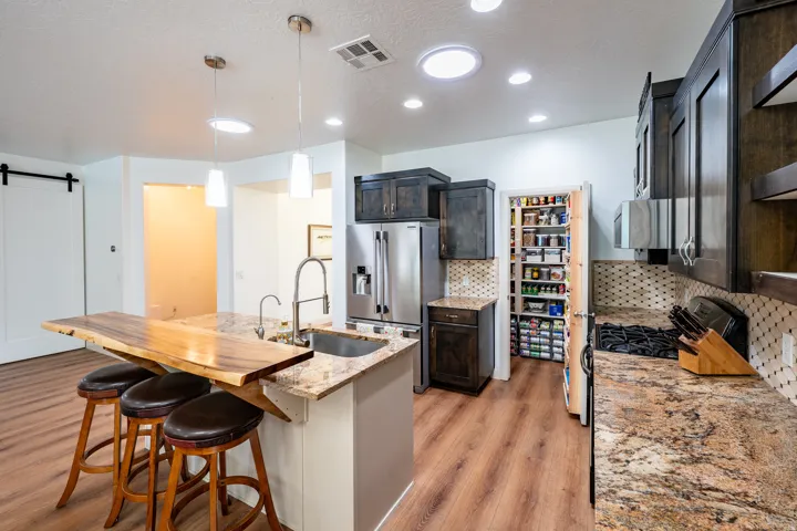 Kitchen featuring granite countertops, dark wood-finish cabinetry, wood-finish flooring, a stainless steel refrigerator, and a walk-in pantry