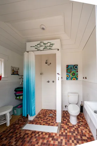 White shiplap ceiling with a recessed light, tiled shower with a chrome fixture, white toilet, and a wall-mounted sink, all set on a mosaic tiled floor