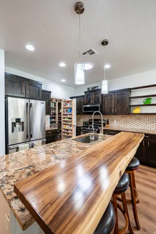 Kitchen featuring dark wood-finish cabinetry, stainless steel appliances, granite countertops, and a live-edge wood island extension